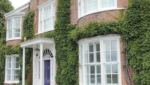 A brick house with white shutters, ivy-covered walls, and a blue door. - The Luxury Annex at Barmby Moor House (York)