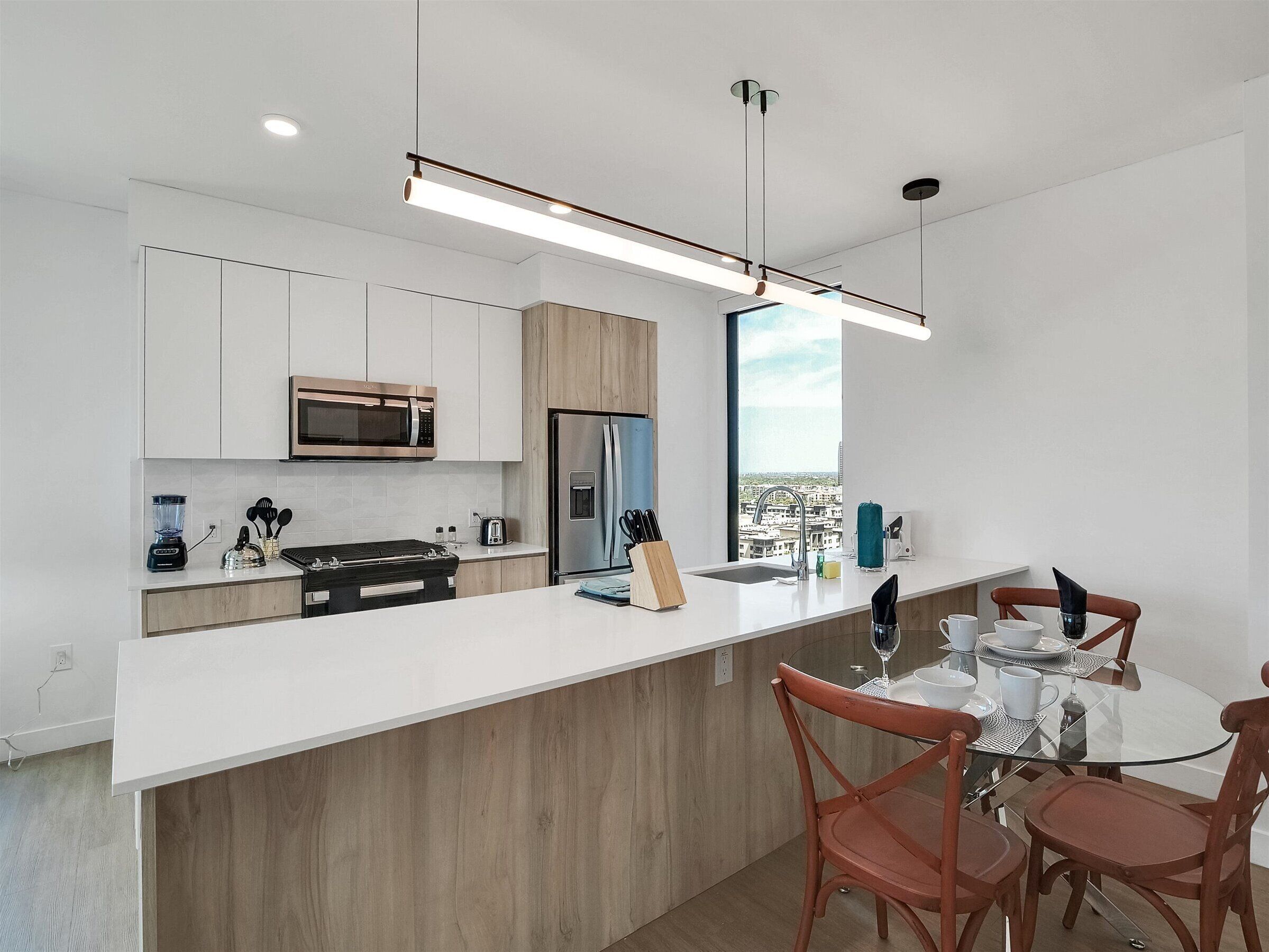 Una cocina moderna con muebles blancos, un refrigerador de acero inoxidable, un microondas y una isla grande con encimera de vidrio.