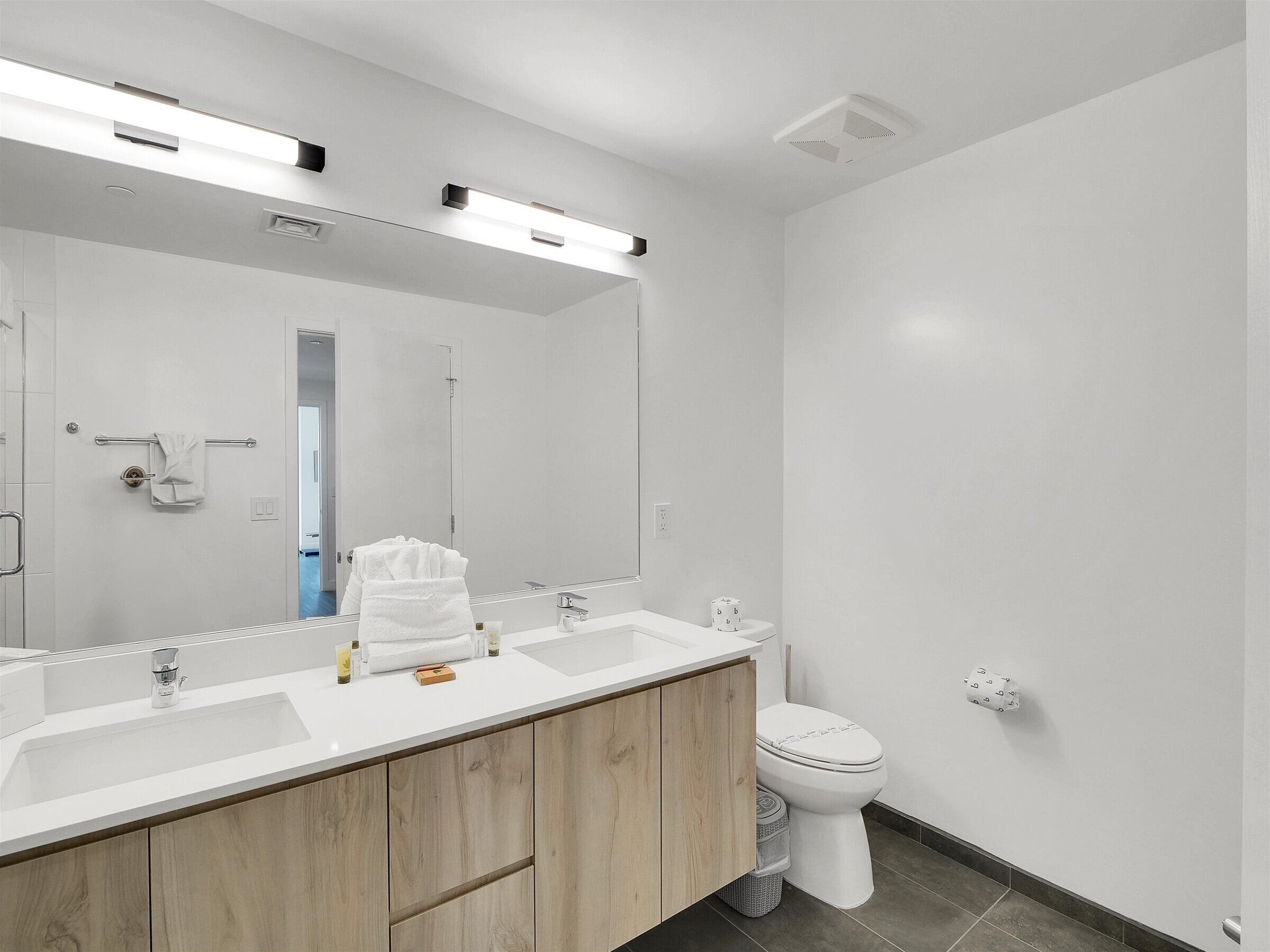 Een moderne badkamer met een grote spiegel, twee wastafels, een toilet en een douchecabine.