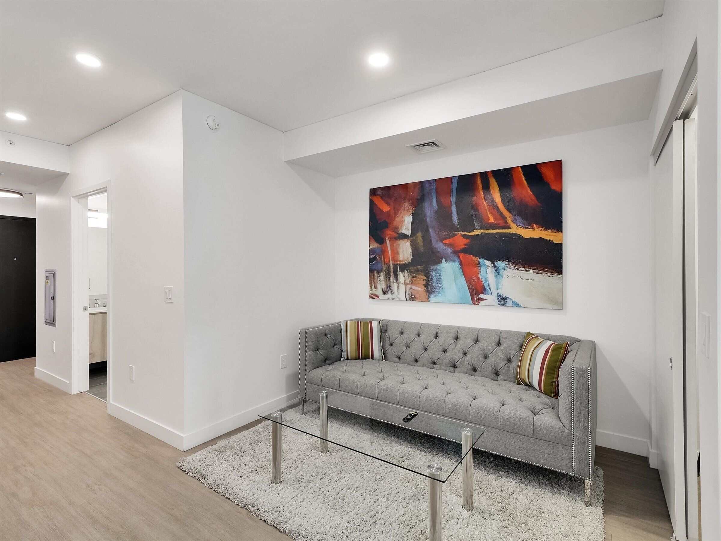 A modern living room with a grey sofa, a glass coffee table, and a large abstract painting on the wall.