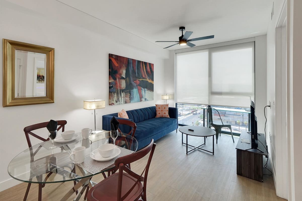 A modern living room with a glass dining table, blue sofa, and a ceiling fan.