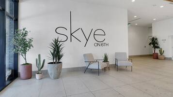 A modern reception area with a large wall sign reading "Sky on 6th", several potted plants, and two seating areas with chairs.