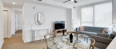 Una sala moderna con una mesa de comedor de vidrio, sillas de madera, un sofá gris y un ventilador de techo.