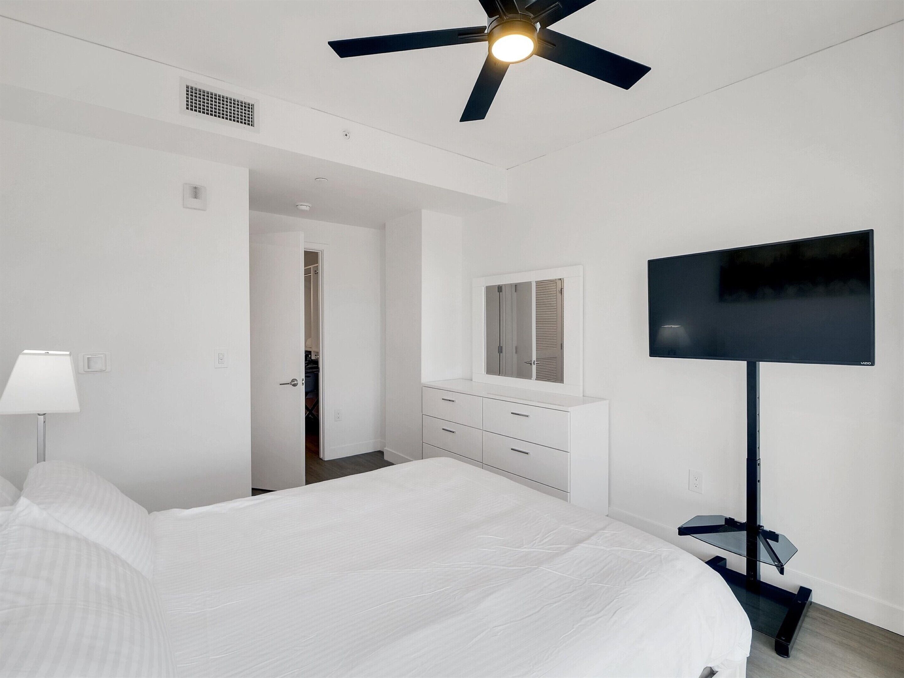 A modern hotel room with a bed, a TV, a ceiling fan, and a walk-in closet.
