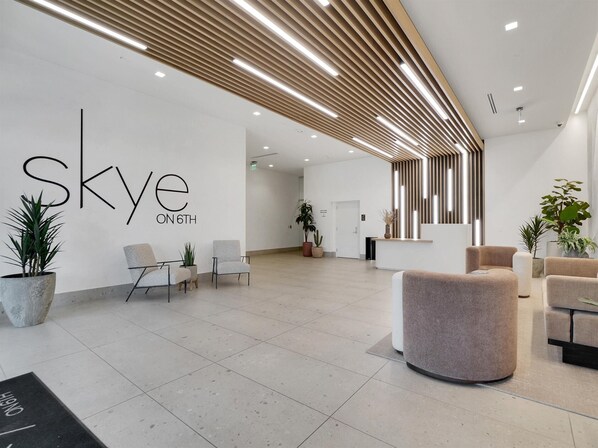 Un espace d’accueil moderne avec un mur blanc où est affiché le titre « Skyline on 6th » et plusieurs options d’assises.