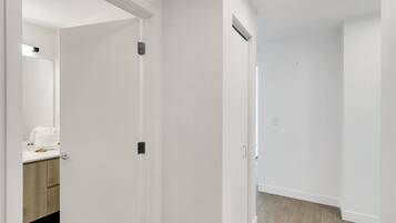 A clean, white-walled hallway with a wooden floor, a bathroom with a mirror and towel, and a door with a handle.