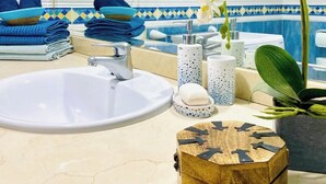 Une salle de bain avec un lavabo blanc, des serviettes bleues, une plante décorative et une boîte en bois.