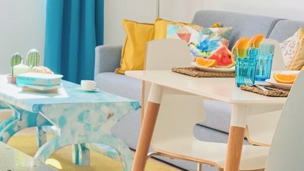 Un salon moderne avec un canapé, une table basse et une table à manger. On y trouve des coussins décoratifs, une lampe sur pied et un tableau accroché au mur.