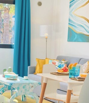 A modern living room with a sofa, a coffee table, and a dining table. There are decorative pillows, a floor lamp, and a painting on the wall. - Casa SILVA, a cozy apartment with fast wi-fi in a calm holiday complex (Corralejo)