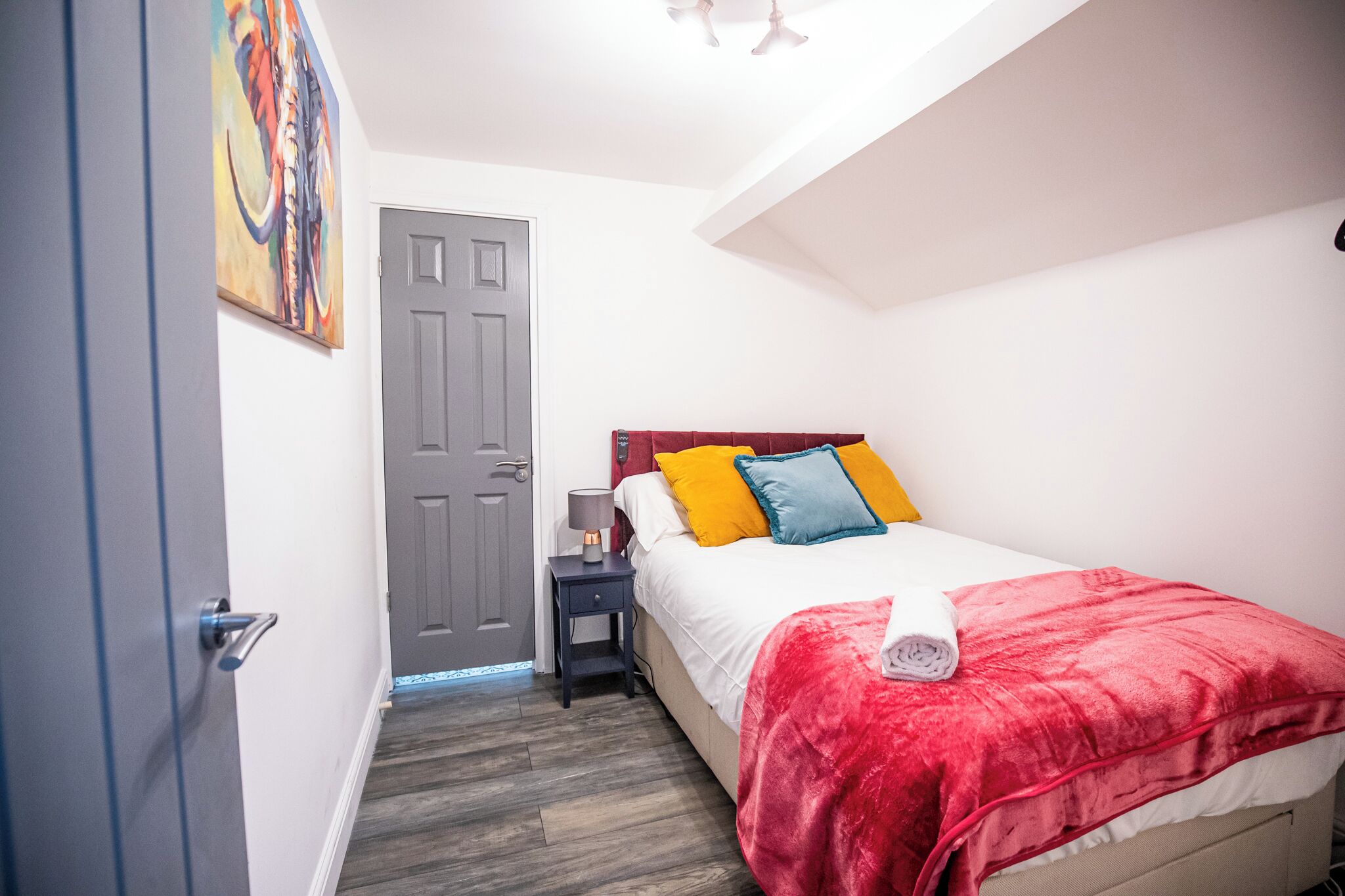 Ein Schlafzimmer mit einem Bett, einem Nachttisch, einer Tür und einem Bild an der Wand.