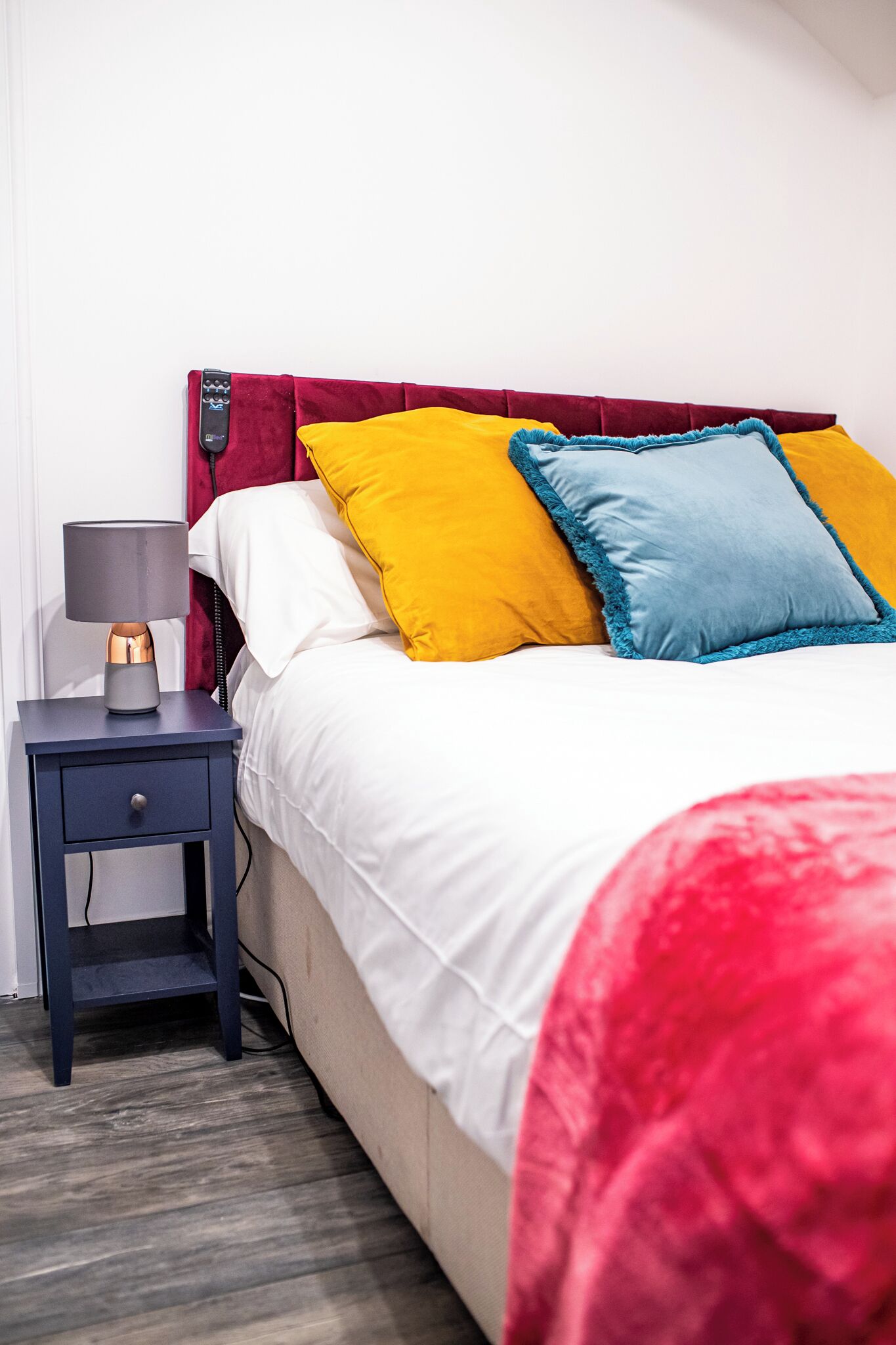 A neatly made bed with white and red bedding, a nightstand with a lamp, and a red headboard.