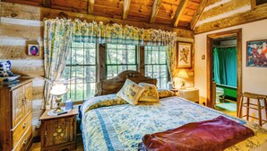 Un dormitorio de cabaña de madera con cama, mesita de noche, cómoda y ventana con cortinas.