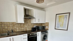 Una cucina con mobili bianchi, un forno a microonde, un fornello e una lavatrice.