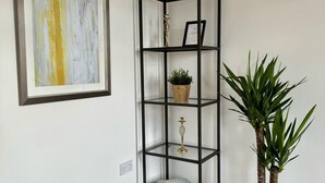 Un angolo di stanza con un'unità scaffale in metallo nero, un quadro astratto incorniciato, una pianta in vaso e un muro bianco.