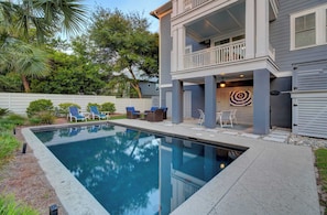 A two-story house with a swimming pool, outdoor seating, and a target decoration.