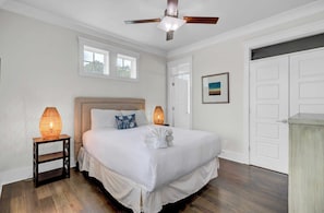 A bedroom with a large bed, two bedside lamps, a ceiling fan, and a door with a view.