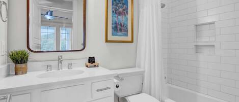 A bathroom with a white sink, mirror, toilet, and bathtub.
