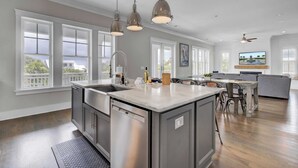 Una cocina amplia con una isla grande, iluminación colgante y una zona de comedor con un sofá gris y un televisor.