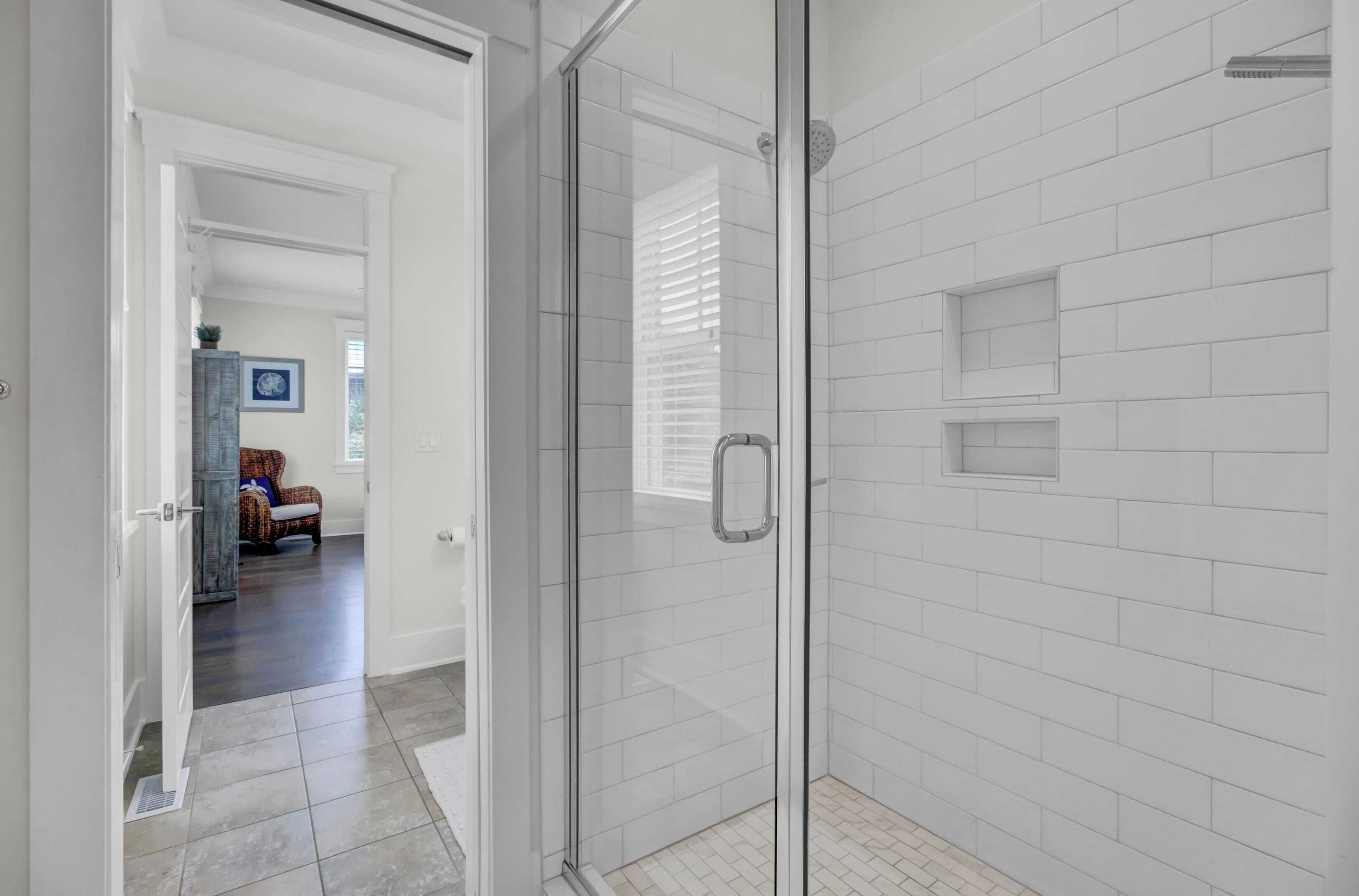 A modern bathroom with white subway tiles, a glass shower enclosure, and a visible hallway leading to a living area.