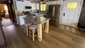A modern kitchen with white cabinets, a stainless steel refrigerator, and a central island with stools. - Lakefront Stay w/ATV Trail Access -Trailer Parking (Iron River)