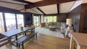 A spacious living area with a wooden bench, sofa, and coffee table. There is a television mounted on the wall and a large window providing natural light. - Lakefront Stay w/ATV Trail Access -Trailer Parking (Iron River)