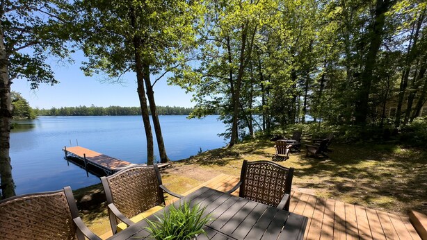 A wooden deck with a table and chairs overlooking a lake, surrounded by trees. - Lakefront Stay w/ATV Trail Access -Trailer Parking (Iron River)