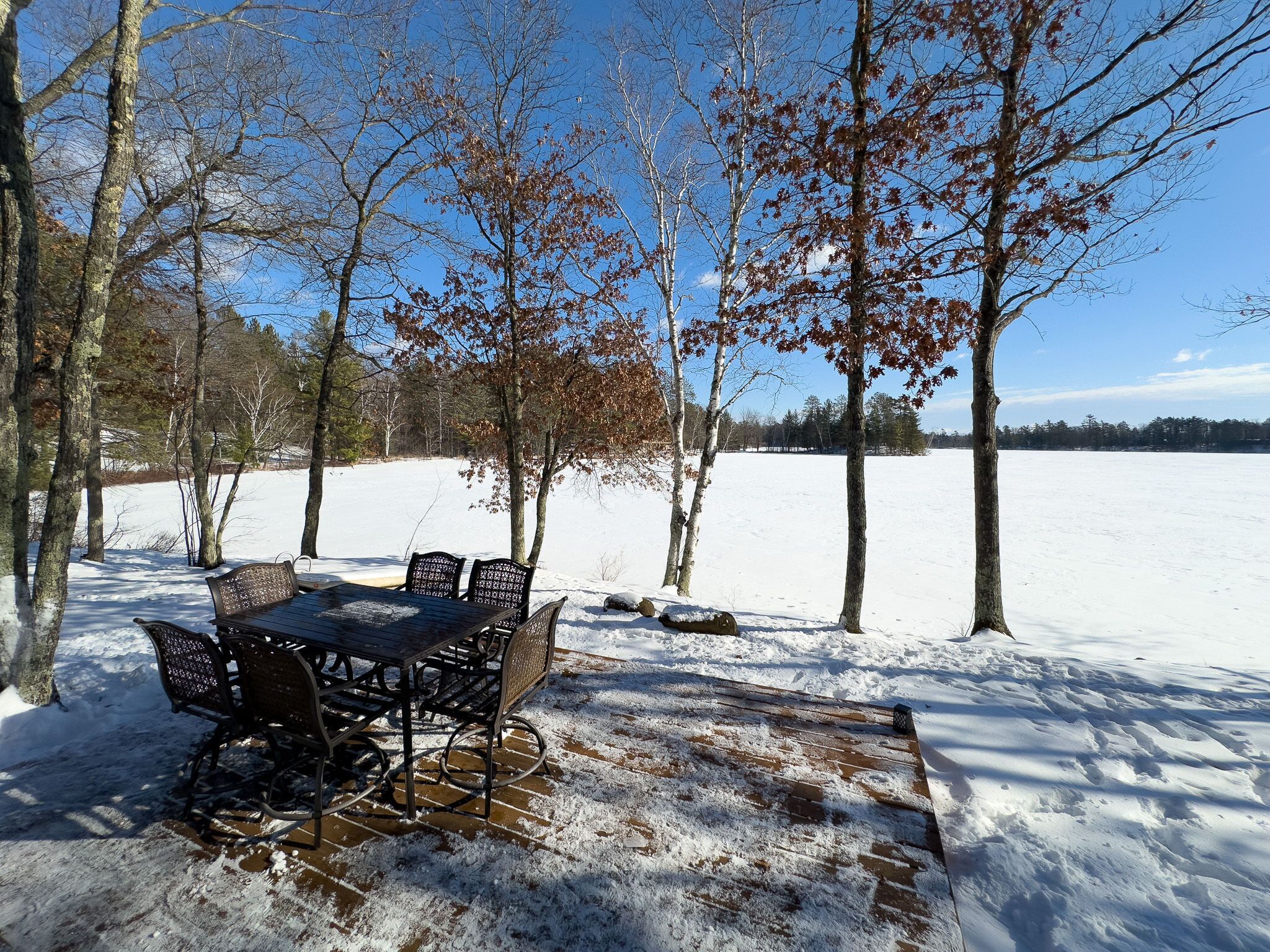 A snow-covered outdoor area with a wooden table and chairs, surrounded by trees.