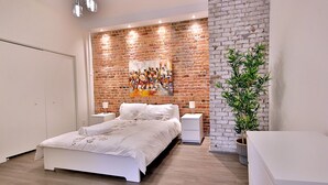 Une chambre moderne avec un mur d’accent en briques, un lit avec une literie blanche, des tables de chevet et une plante en pot.