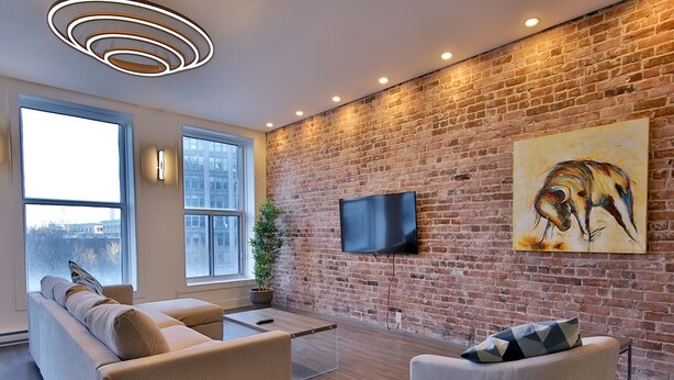 Un salon moderne avec un mur en briques, un téléviseur à écran plat, un canapé, un fauteuil et une grande fenêtre.