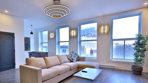 Un salon moderne avec un canapé d’angle beige, une table basse en verre et de grandes fenêtres qui laissent entrer la lumière naturelle.