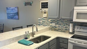 Una cocina moderna con lavavajillas integrado, un lavamanos de acero inoxidable y un microondas.