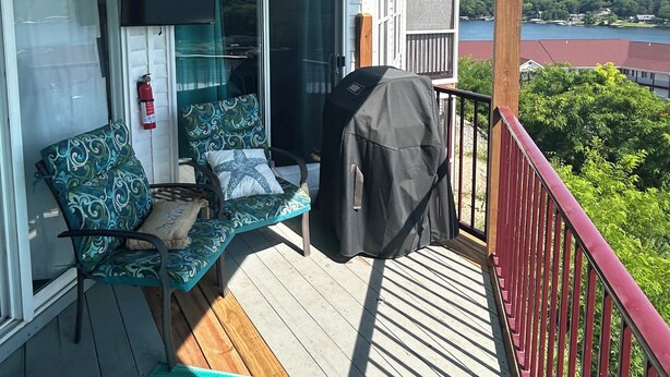 Una terraza techada con ventilador de techo, televisor montado en la pared, mobiliario exterior con cojines y una parrilla.