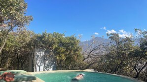 A swimming pool with a person swimming, surrounded by trees and a mountain view. - Suite Flotante: glass carpet floor and magical views (Oaxaca de Juárez)