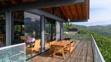 A modern outdoor deck with a wooden table and chairs, a hanging planter, and a view of the surrounding landscape.