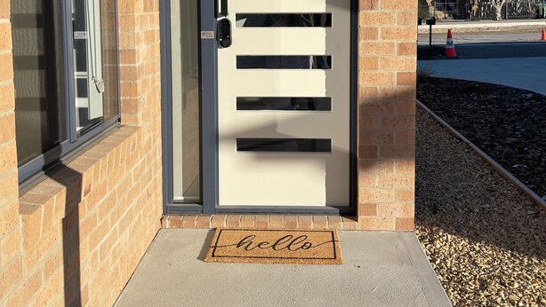 A modern door with horizontal slats and a keypad lock, set in a brick wall with a clear view of the driveway and a doormat with "hello" written on it. - Home away from home in Brighton (Brighton)