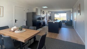 A modern kitchen with dark cabinetry, a central island, and a dining area with a wooden table and chairs. - Home away from home in Brighton (Brighton)