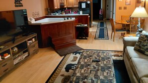 Una sala de estar con televisor, sofá y un área de cocina con armarios de madera y refrigerador.