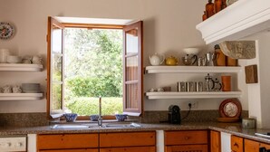 A kitchen with a window, wooden cabinets, and various kitchenware on shelves. - Almancil Sea and Countryside Secluded Villa (Loulé)