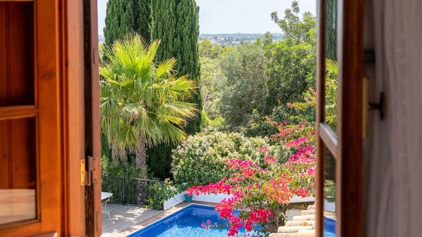 An open door leading to a balcony with a pool, surrounded by greenery and cypress trees. - Almancil Sea and Countryside Secluded Villa (Loulé)