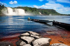 Una barca ormeggiata su una riva rocciosa con una cascata sullo sfondo.