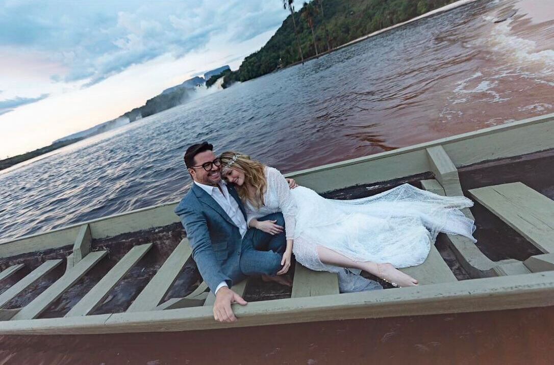 Un couple, vêtu pour un mariage, se trouve sur un bateau en bois au bord d’une rivière.