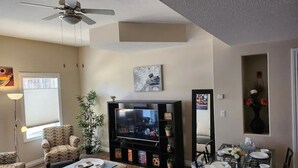 A living room with a television, seating, a dining area, and a ceiling fan.