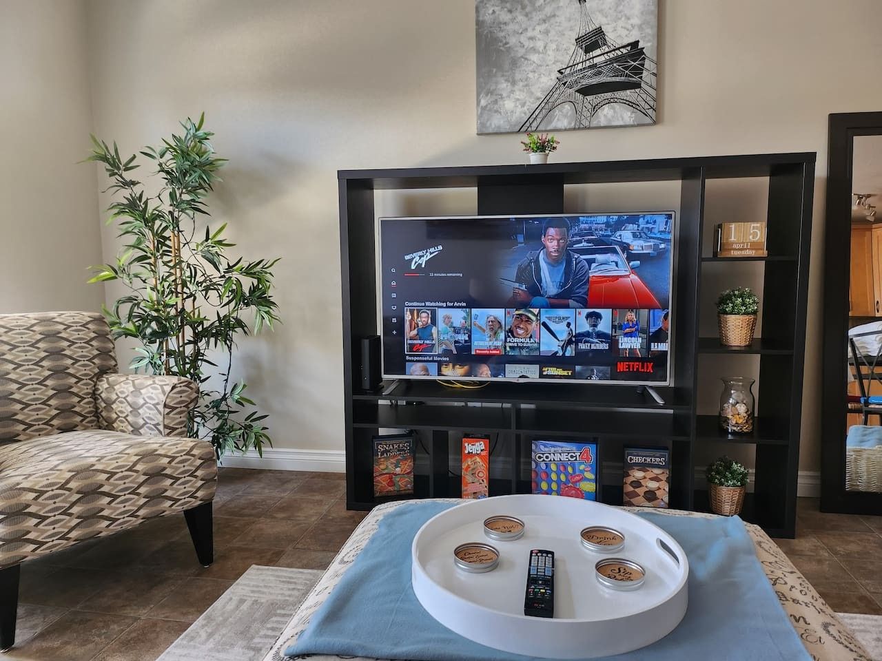 Ein Wohnzimmer mit Fernseher, der eine Streaming-Dienstanwendung anzeigt, einer Couch, einem Couchtisch mit Fernbedienungen und einer Zimmerpflanze.