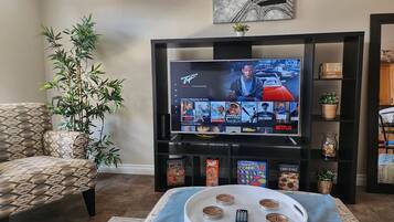 Ein Wohnzimmer mit Fernseher, der eine Streaming-Dienstanwendung anzeigt, einer Couch, einem Couchtisch mit Fernbedienungen und einer Zimmerpflanze.
