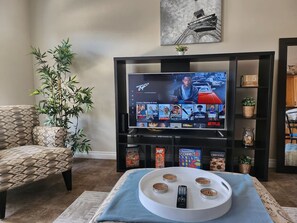 A living room with a television displaying a streaming service interface, a sofa, a coffee table with remote controls, and a decorative plant.