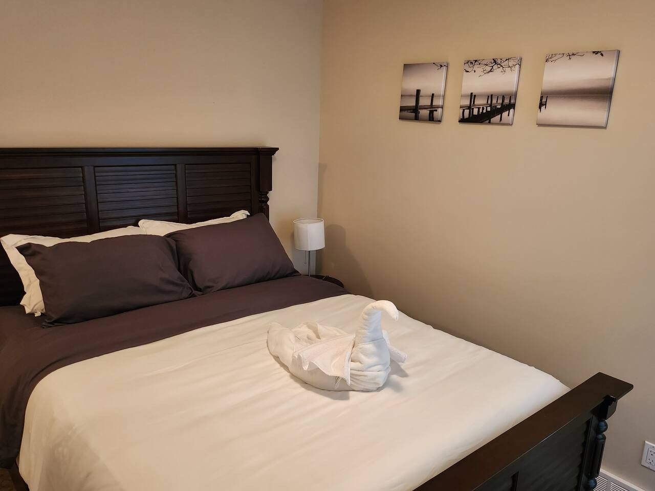 A hotel room with a bed, pillows, a headboard, a nightstand, a lamp, and wall art.