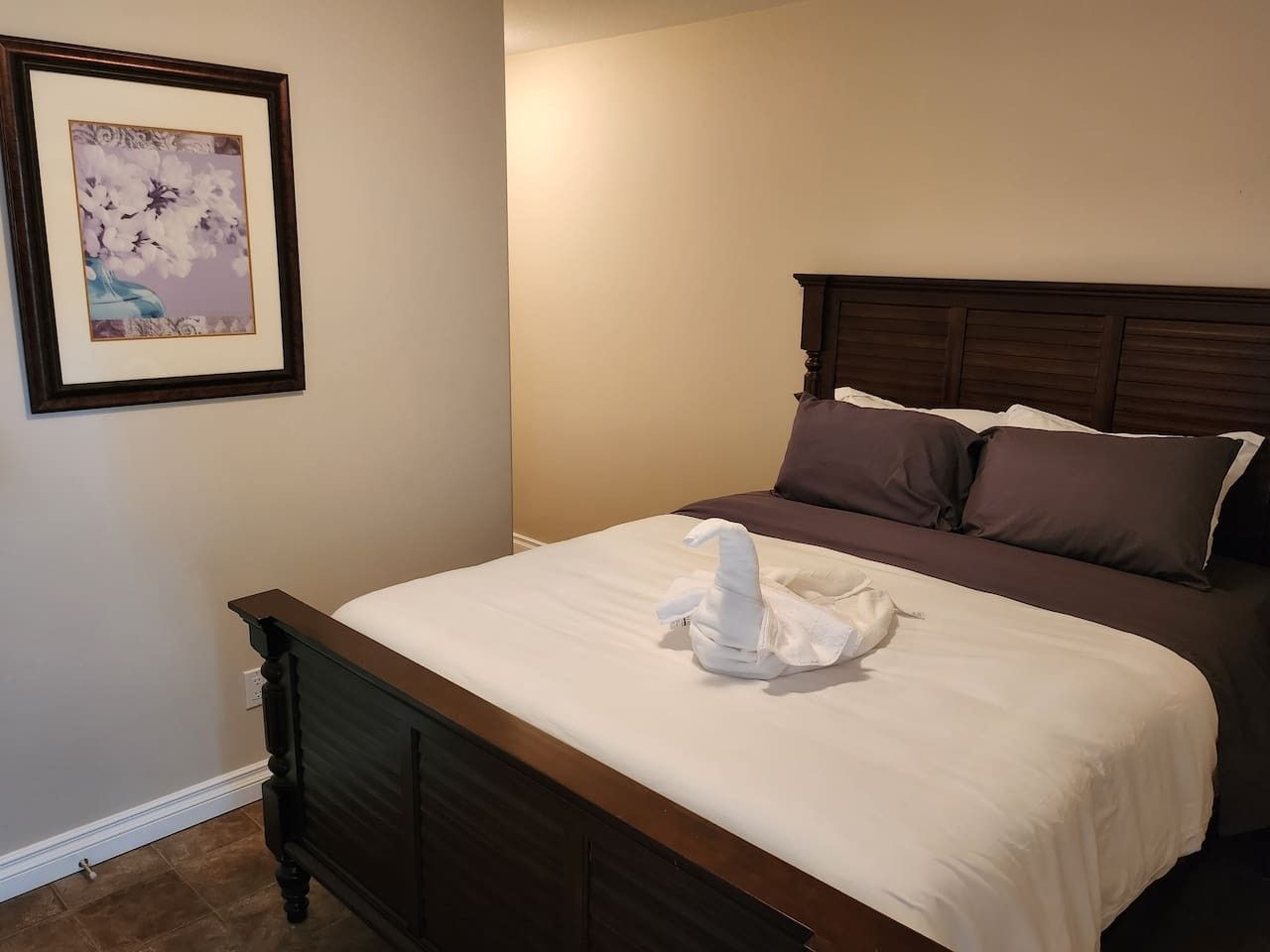 A neatly made bed with a white comforter and pillows, a framed picture on the wall, and a wooden headboard.