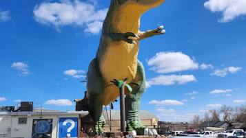 Een grote opblaasbare dinosaurus in een parkeerplaats, met auto's en een gebouw op de achtergrond.