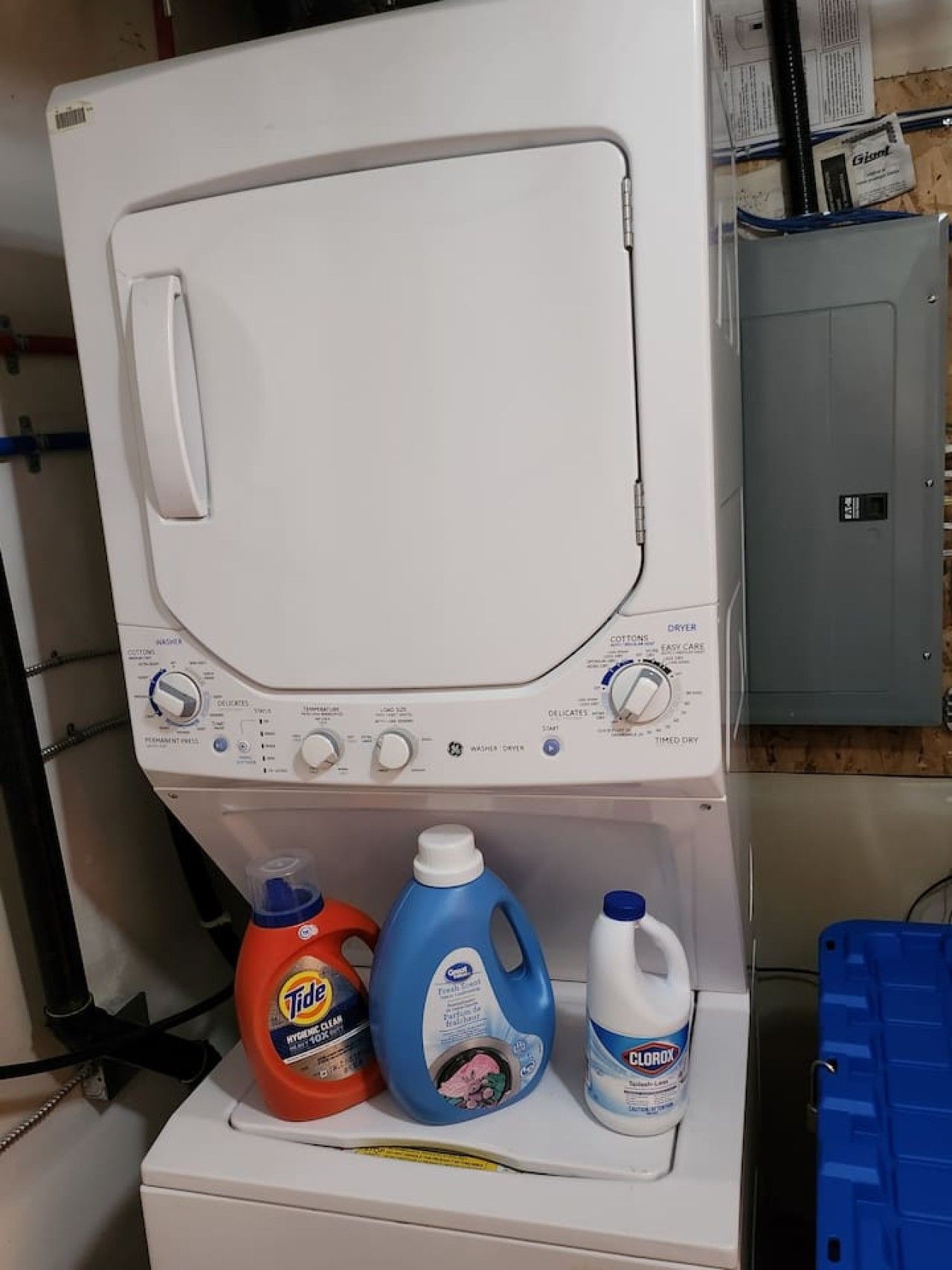 A front-loading washing machine with detergent bottles on the lower shelf.