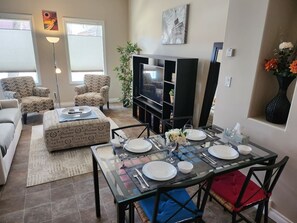 Een eetruimte met een glazen tafel gedekt voor vier personen, omringd door fauteuils met een patroon en een bank.